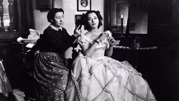 Cathy (Merle Oberon) seated in a gown while Ellen Dean (Flora Robson) fixes her hair