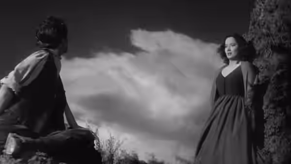 Heathcliff (Laurence Olivier) seated on rocks facing Cathy (Merle Oberon) standing