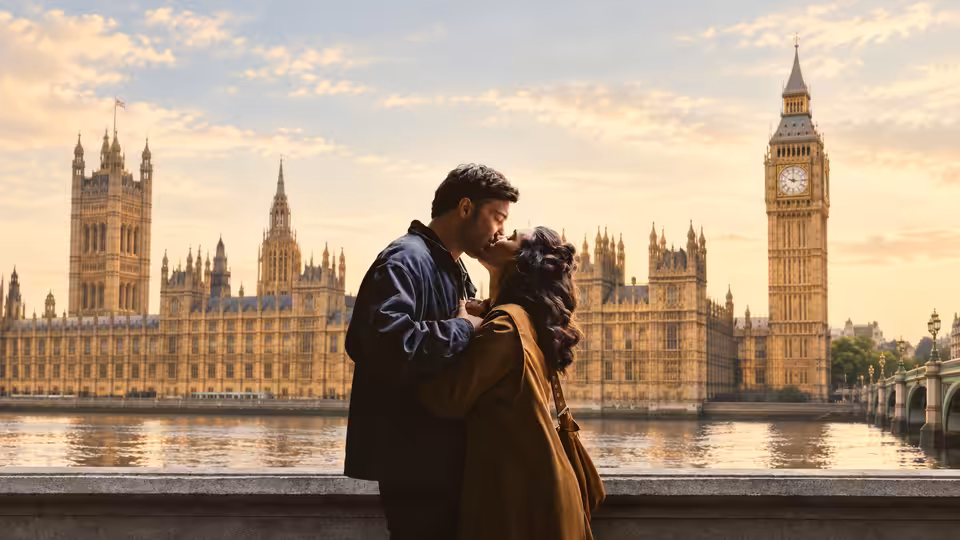 A couple kiss beside the Thames, with the Houses of Parliament and Elizabeth Tower behind them