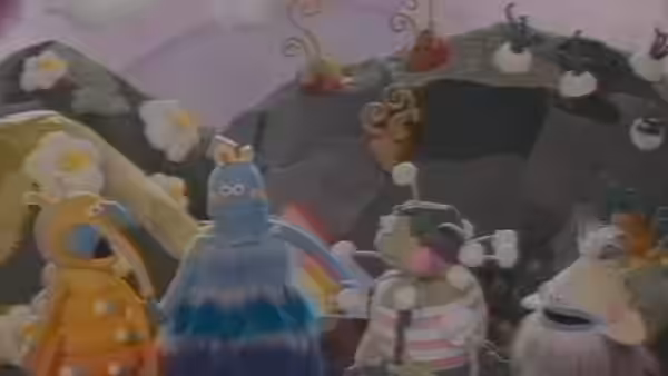 A group of colorful puppet characters stand together against a painted garden backdrop