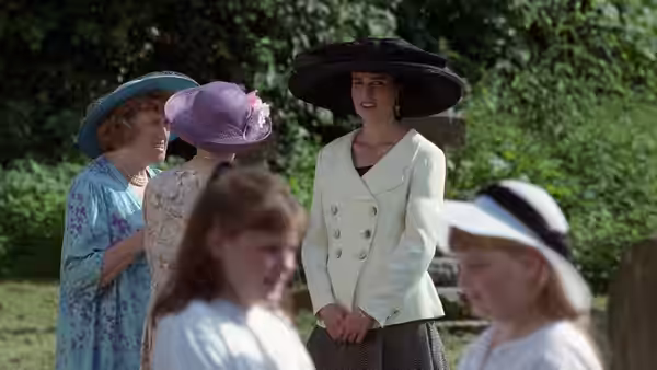 Carrie (Andie MacDowell) in a pale suit smiles among women wearing hats