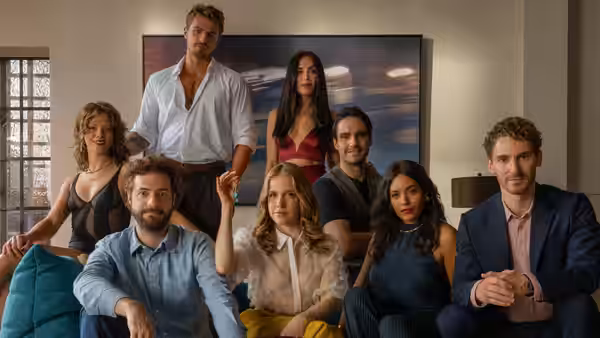 Eight adults gather around a sofa in a living room, facing forward