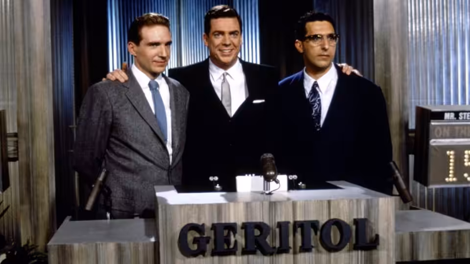 Three suited men stand behind a Geritol desk in a television studio