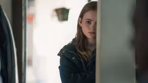 Ellie (Sadie Sink) peers from behind a doorway into the apartment