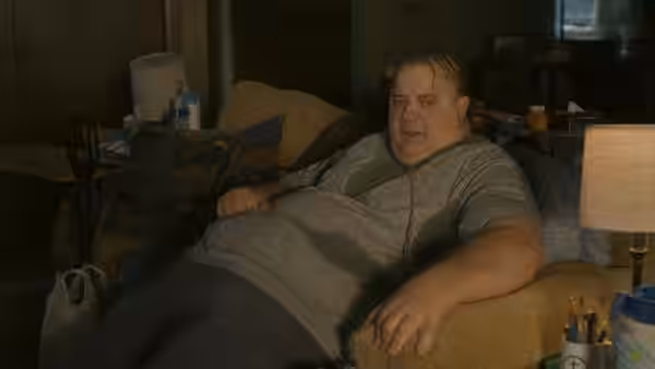 Charlie (Brendan Fraser) reclines on a couch in his cluttered apartment