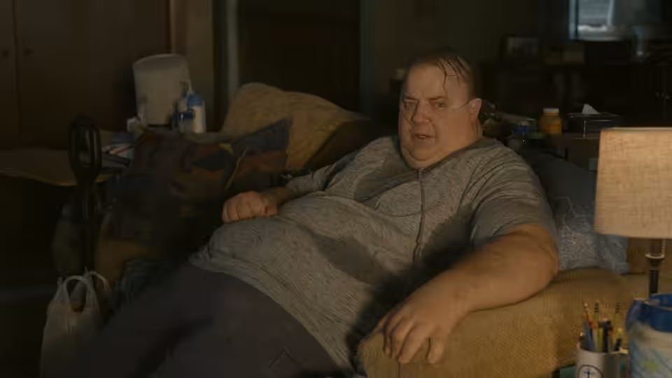 Charlie (Brendan Fraser) reclines on a couch in his cluttered apartment