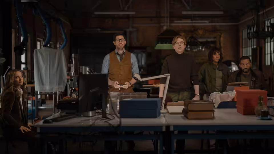 A group gathers around a cluttered workbench in a crowded workshop