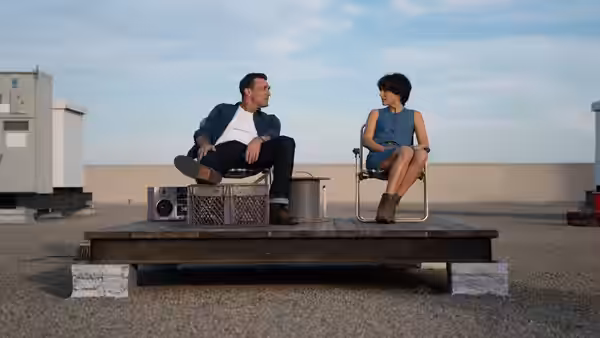 Lucy Cola (Natalie Portman) and Mark Goodwin (Jon Hamm) sit together on a rooftop platform