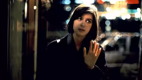 Valentine (Irène Jacob) standing at a glass door on a city street at night