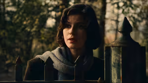 Valentine (Irène Jacob) wearing a scarf and standing by a metal fence outdoors