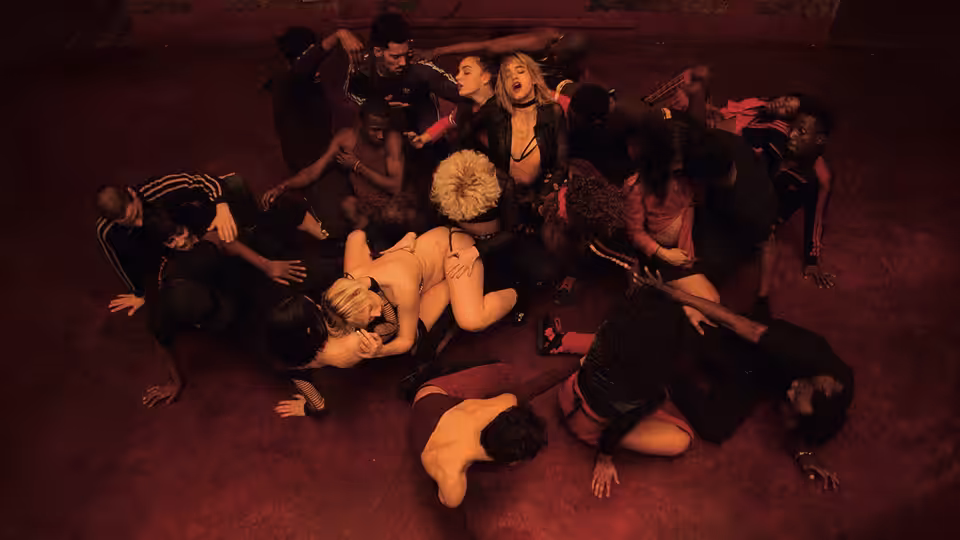 A crowd of people lies entangled on a red-lit floor
