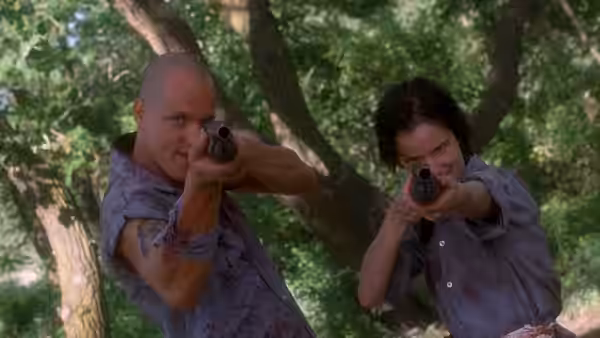 Mickey Knox (Woody Harrelson) and Mallory Knox (Juliette Lewis) aiming pistols in woods