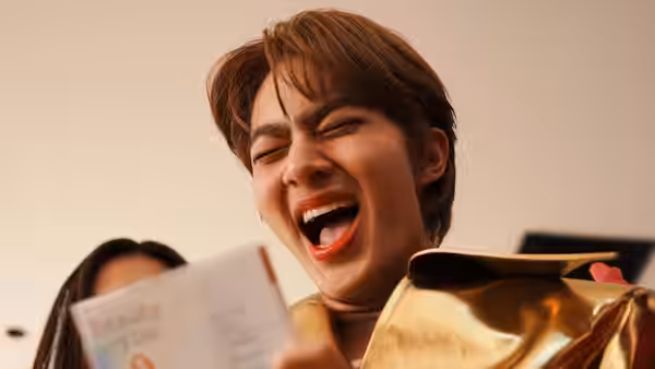 A young man sings with his eyes closed, holding a paper beside a gold jacket