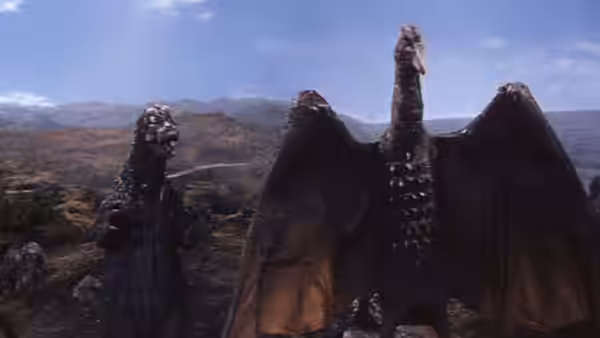 Godzilla faces King Ghidorah across a rocky landscape beneath a cloudy sky