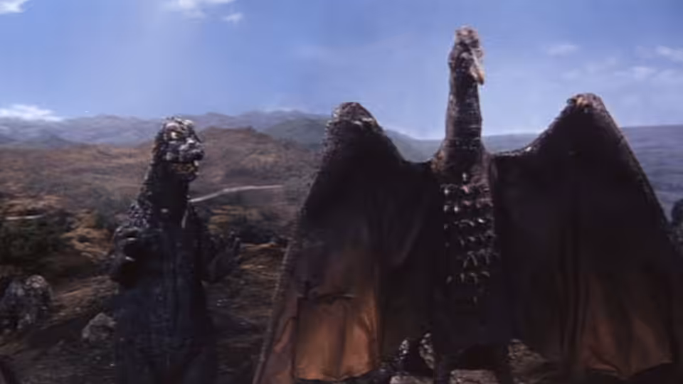 Godzilla faces King Ghidorah across a rocky landscape beneath a cloudy sky