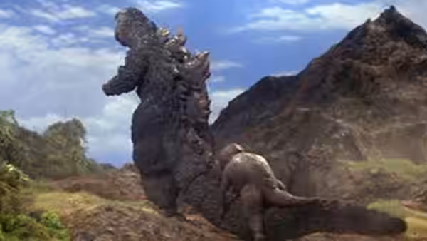 Godzilla stands over a fallen giant creature in a mountain valley