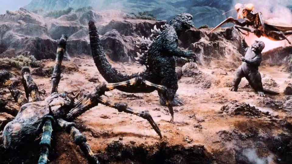 Godzilla battles a giant praying mantis as another monster approaches across rocky terrain