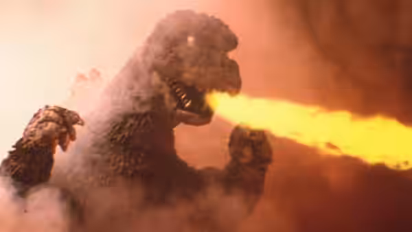 Godzilla breathes a stream of fire through smoke, raising both arms