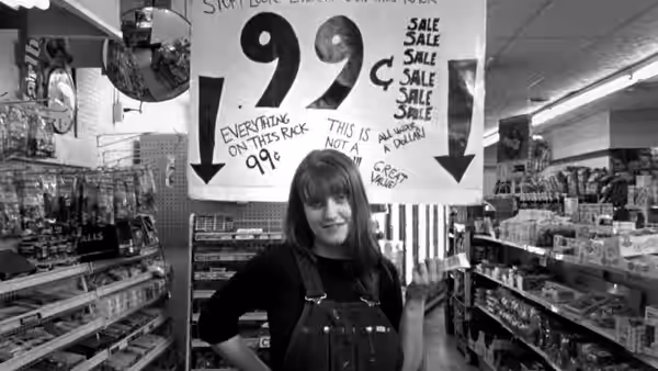 A woman standing in a video store beneath a large sale sign