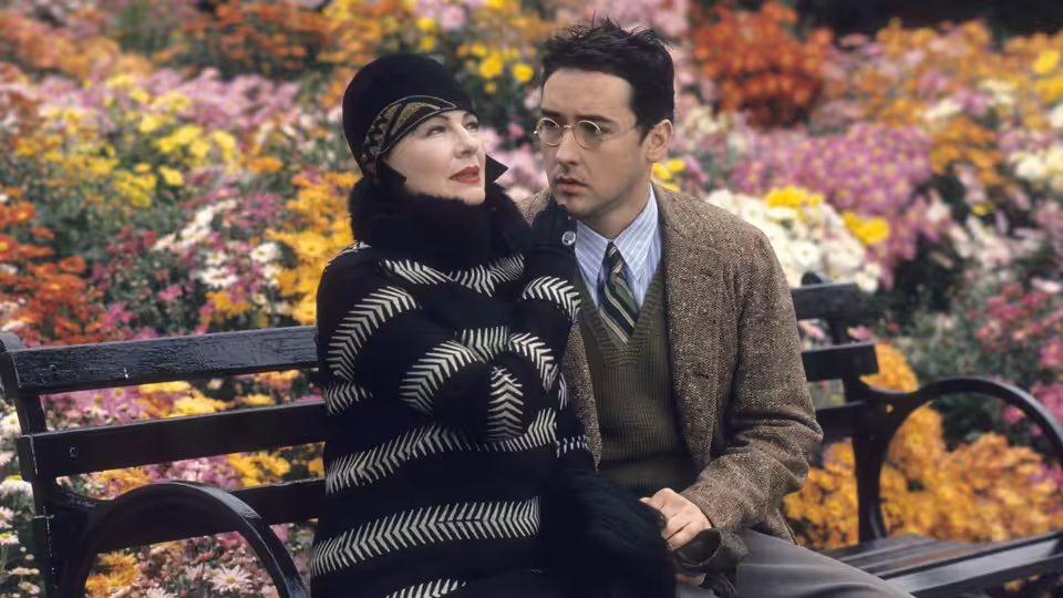David Shayne (John Cusack) sits with Helen Sinclair (Dianne Wiest) on a bench amid colorful flowers