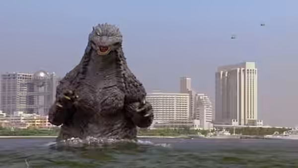 Godzilla wades out of the water toward a city skyline