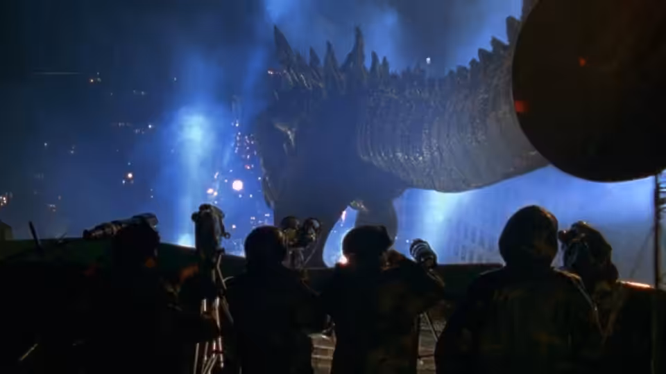 People look up at Godzilla looming over them in a blue-lit city