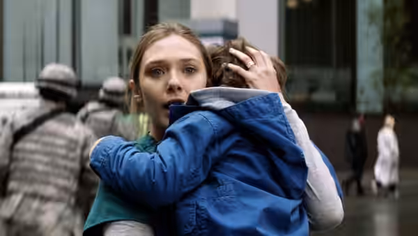 Elle Brody (Elizabeth Olsen) holds a child close as soldiers pass behind them