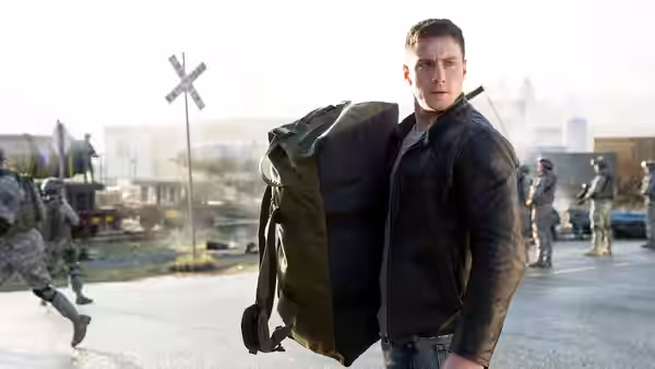 Ford Brody (Aaron Taylor-Johnson) carries a large bag through a military staging area