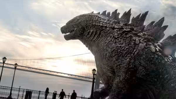 Godzilla towers over people on a waterfront promenade at sunset