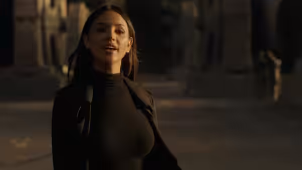 Maia Simmons (Eiza Gonzalez) stands in a dim stone courtyard