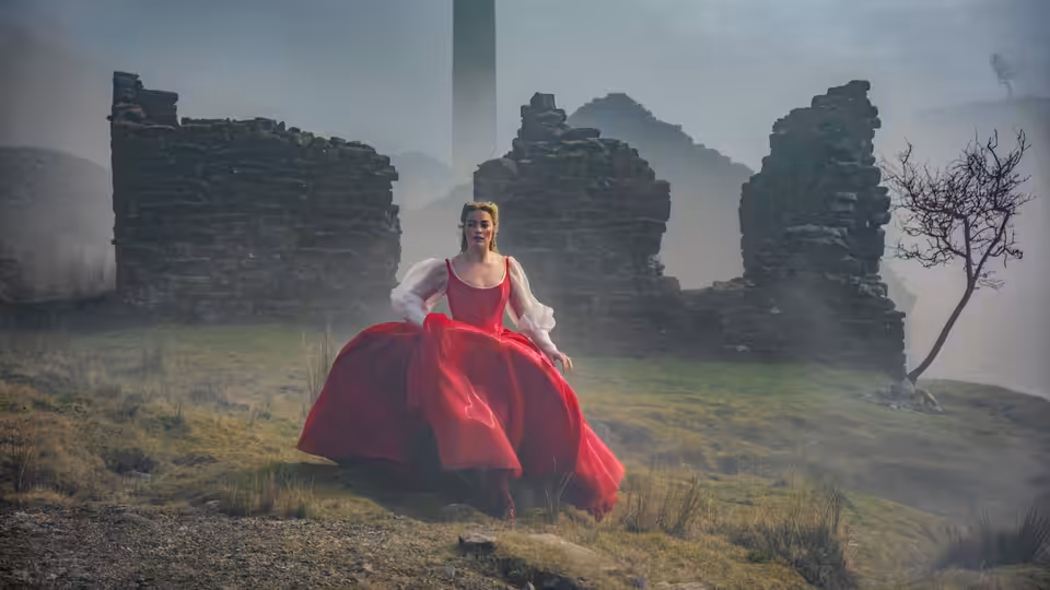 Cathy (Margot Robbie) sits in a red gown among the mist-shrouded ruins