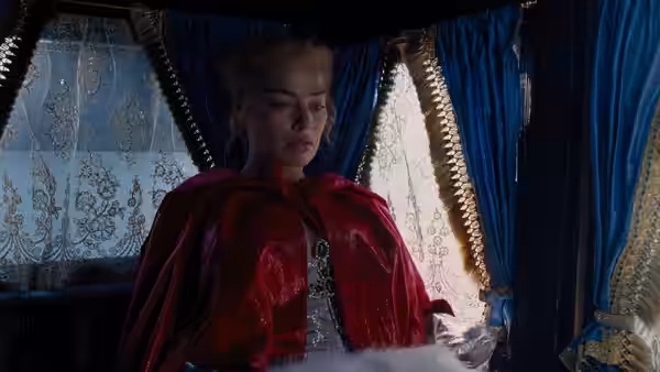 Cathy (Margot Robbie) sits inside a curtained carriage wearing a red cloak