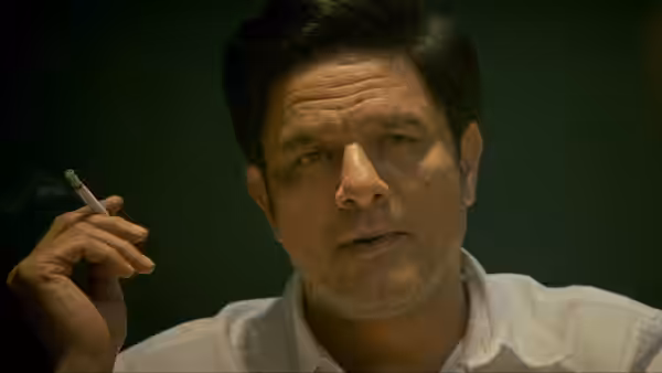 A man in a white shirt holds a cigarette while looking forward