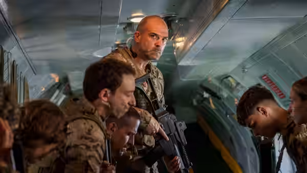 Armed men crouch inside an aircraft cabin as a bald soldier holds a rifle