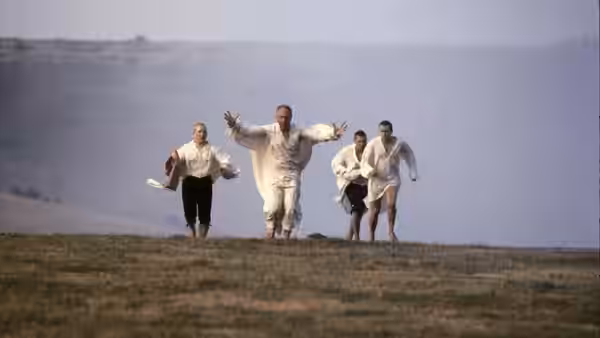 three men in white shirts running across a grassy hillside with arms outstretched