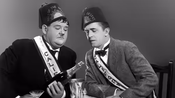 Stan (Stan Laurel) and Ollie (Oliver Hardy) inspect a bottle together at the table