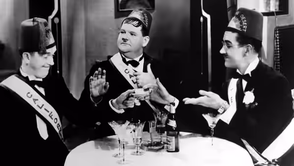 Stan (Stan Laurel), a fellow lodge member, and Ollie (Oliver Hardy) gather around drinks at a table
