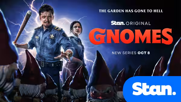 A uniformed man raises a wooden bat as a woman and angry garden gnomes gather