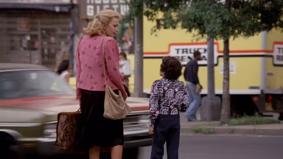 Gloria (Gena Rowlands) stands on a street beside young Phil with a suitcase