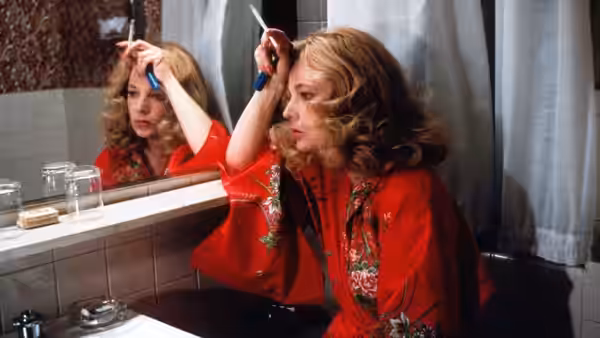 Gloria (Gena Rowlands) trims her hair with scissors in a bathroom mirror