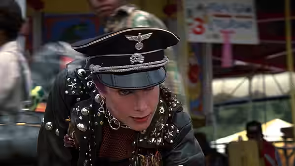 A woman in a studded jacket and military cap leans forward