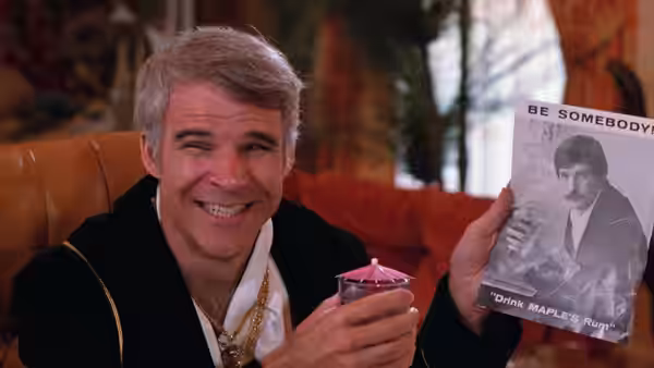 Navin (Steve Martin) holds up a rum advertisement while smiling with a drink