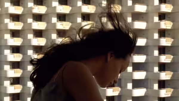 Woman with long dark hair in front of a large apartment building