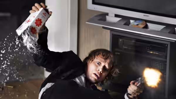 Roger Brown (Aksel Hennie) fires a gun while falling beside a kitchen oven