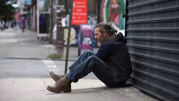 Joe (Joaquin Phoenix) sitting on the sidewalk against a metal shutter