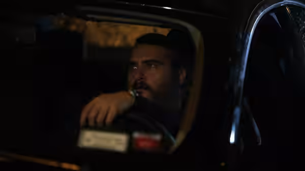 Joe (Joaquin Phoenix) driving a car at night with arm on the wheel
