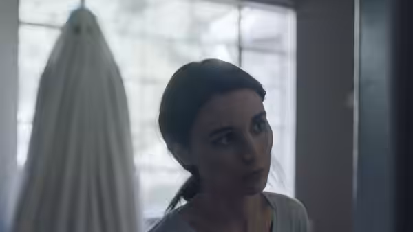 M (Rooney Mara) standing near a window with a ghost behind her