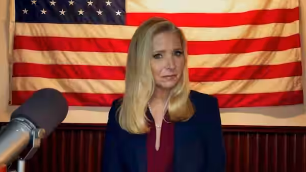 Jeanetta Grace Susan (Lisa Kudrow) sits before an American flag beside a microphone