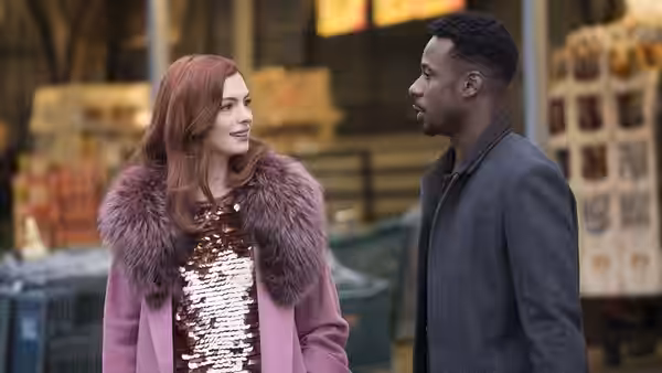 A red-haired woman in a fur-trimmed coat talks with a man on a city sidewalk