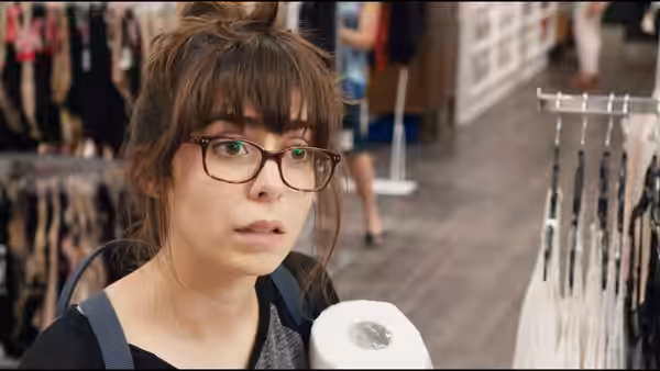 Sonia Friedman (Cristin Milioti) wears glasses and a backpack while browsing clothes in a store